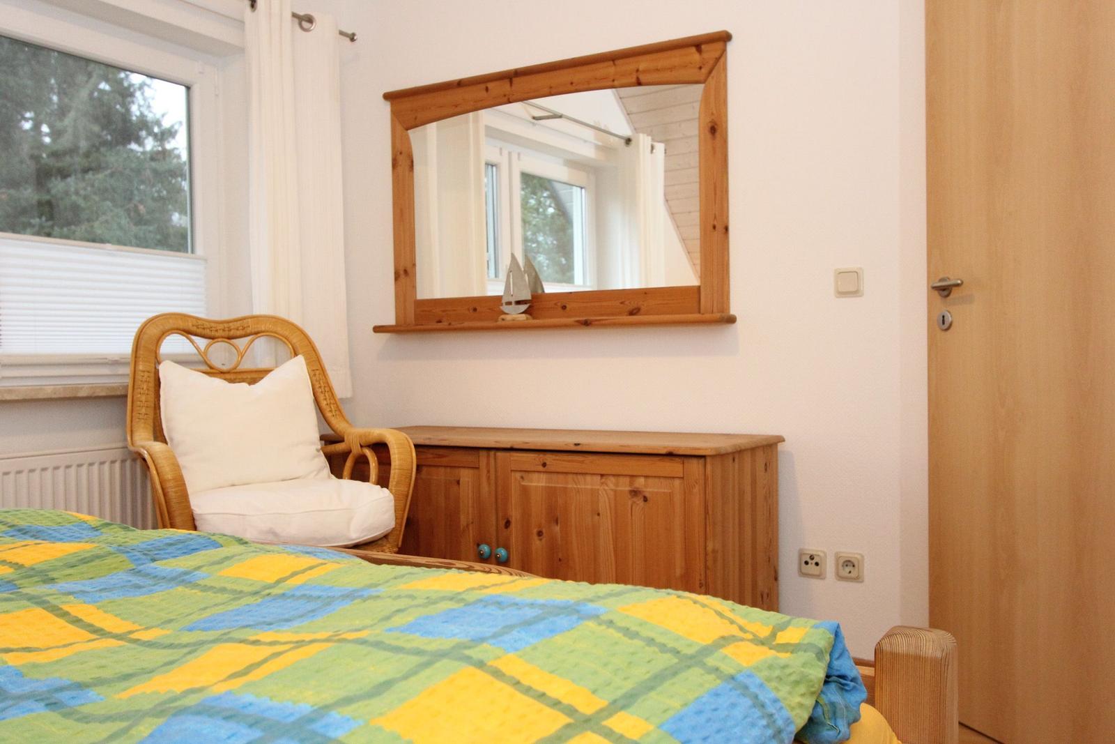 Schlafzimmer mit Bett, Stuhl, Spiegel und Holzschränkchen.