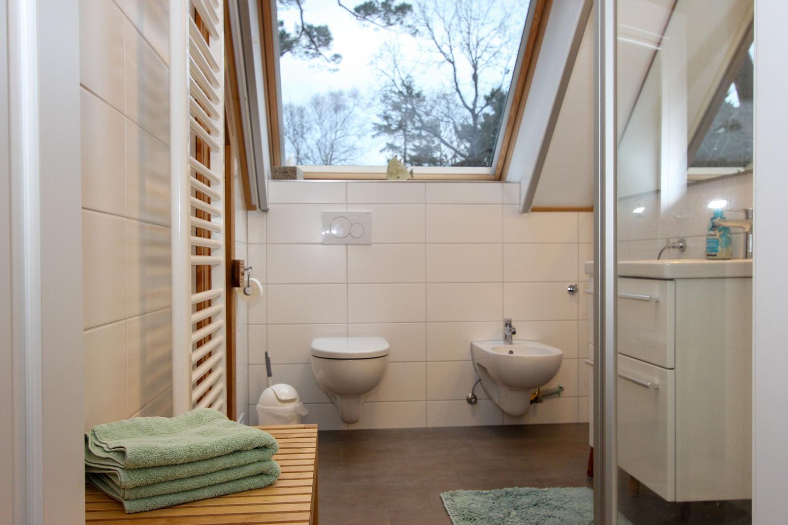 Badezimmer mit Toilette, Waschbecken und Dusche. Fenster mit Blick auf Bäume.