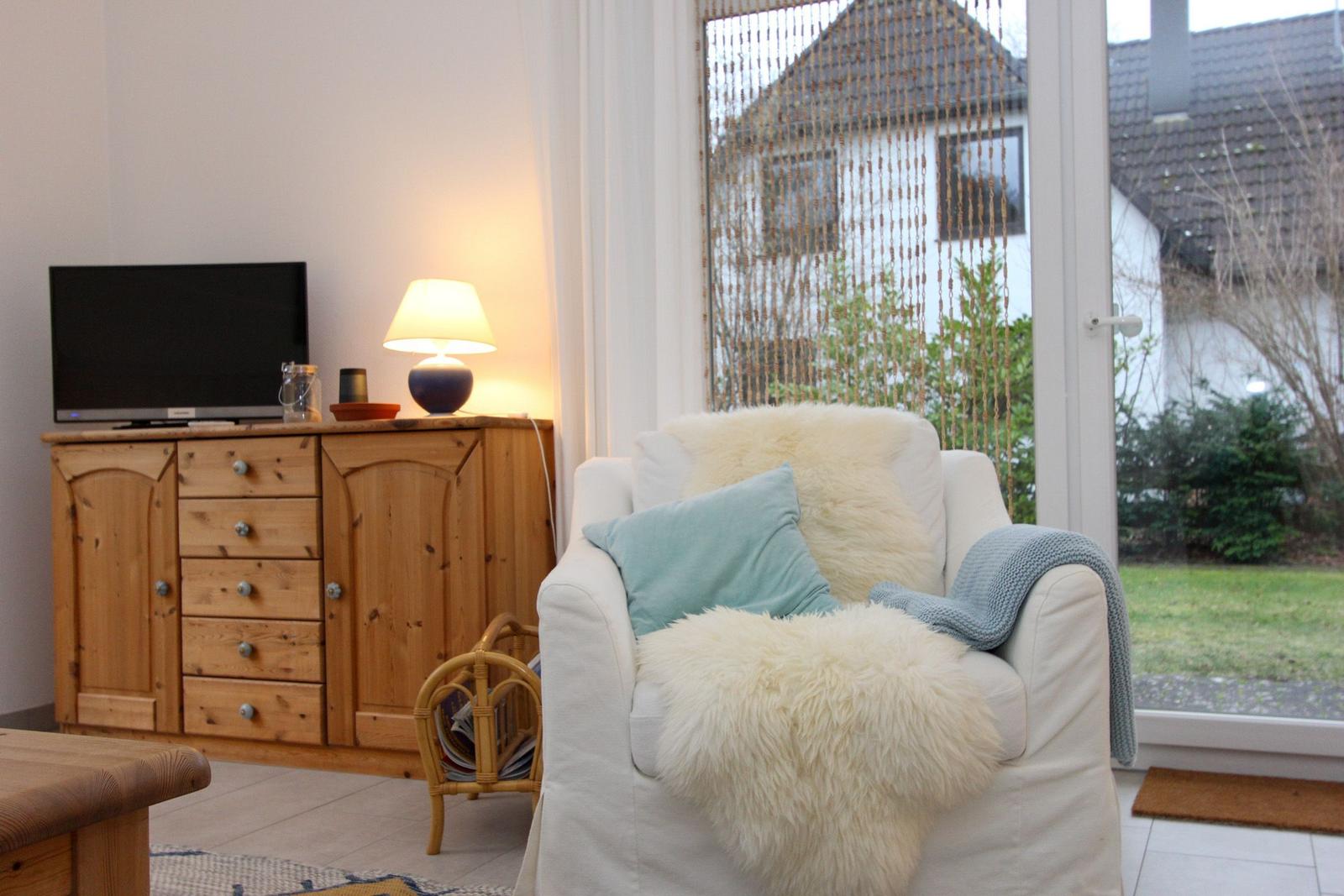 Weißer Sessel mit Felldecke und Kissen, Holzschrank mit Fernseher und Lampe.