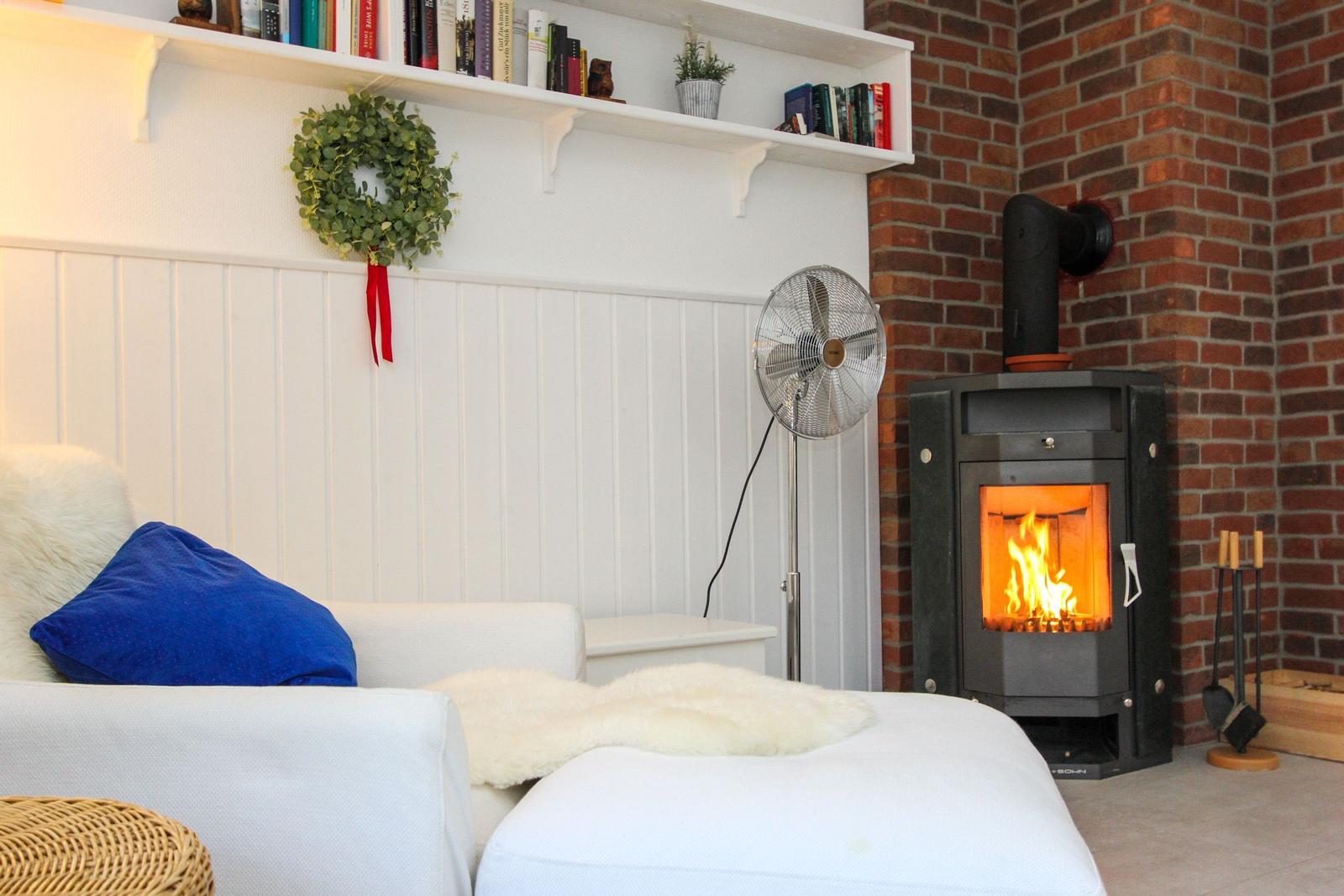 Wohnzimmer mit Kaminofen, weißen Wänden, Bücherregal und Sitzgelegenheit.