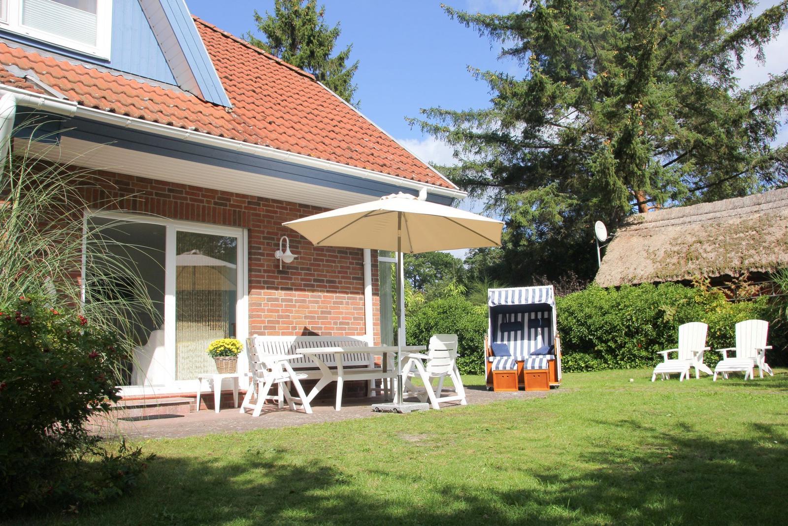 Haus mit Terrasse, Gartenmöbeln und Strandkorb unter einem Sonnenschirm.