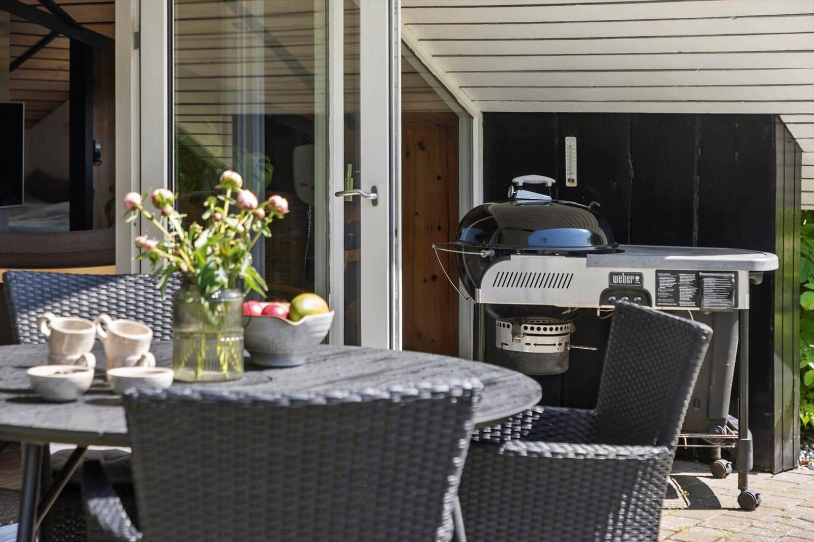 Terrasse mit Tisch, Stühlen, Grill und Blumenarrangement.