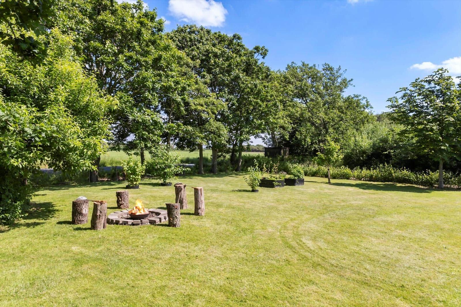 Grüner Garten mit Feuerplatz und Baumstumpf-Sitzgelegenheiten unter Bäumen.