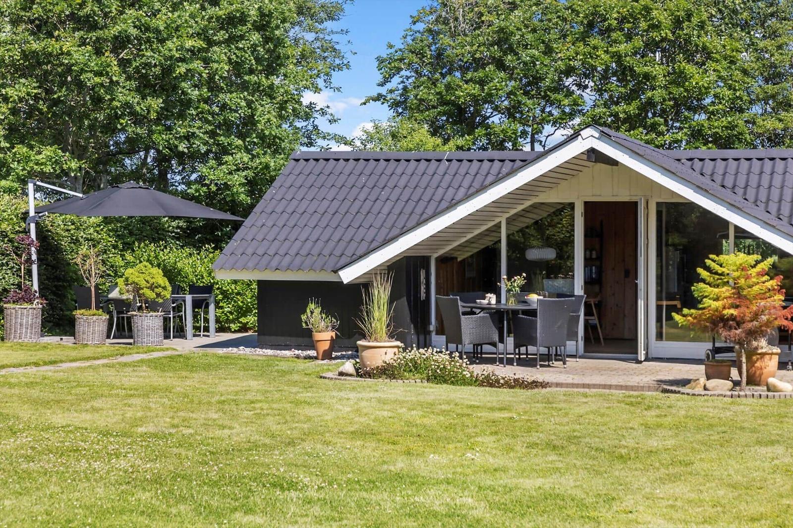 Moderne Hütte mit Terrasse, Garten und Sitzgelegenheiten unter einem Sonnenschutz.