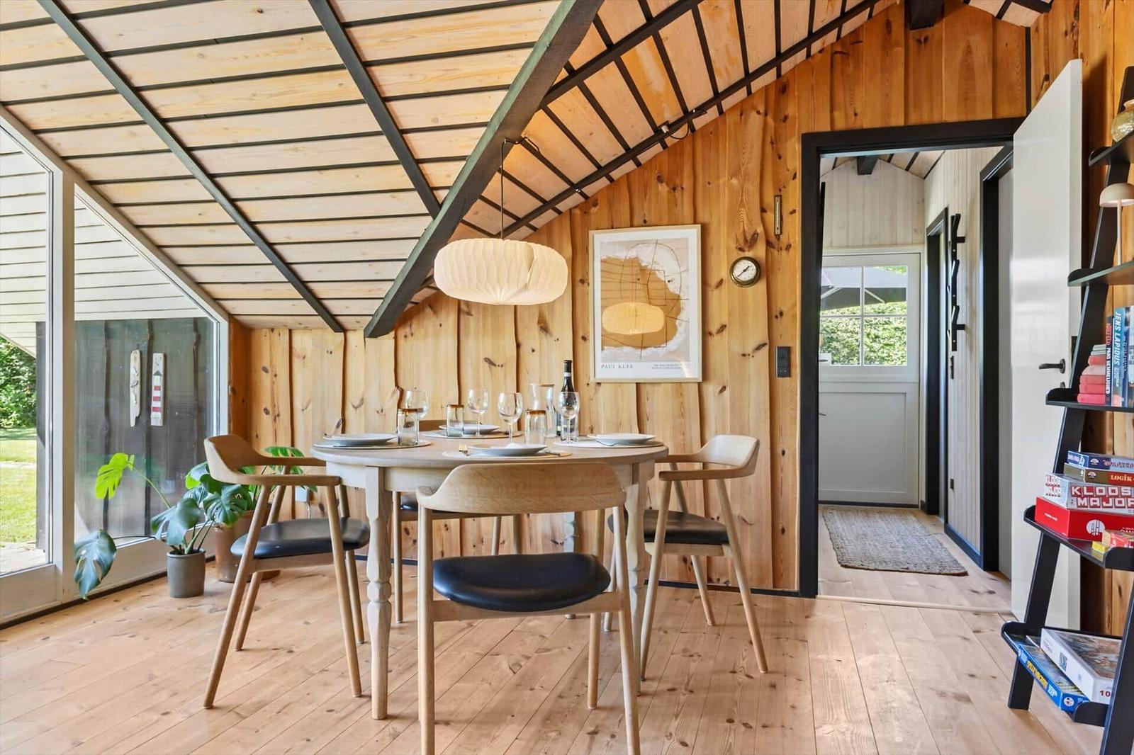 Esszimmer mit Holzwand, Tisch und Stühlen, Glasfront und Bücherregal.