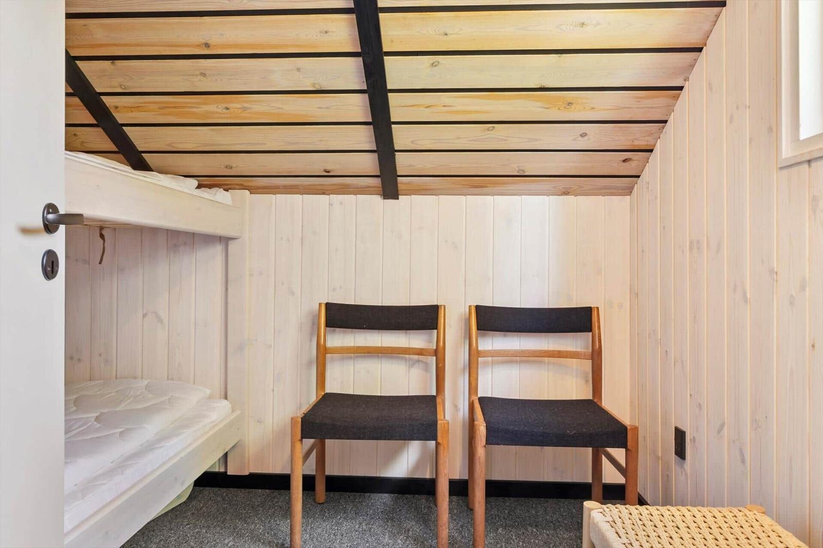 Zimmer mit Schlafcouch, zwei Stühlen und Holzwänden.