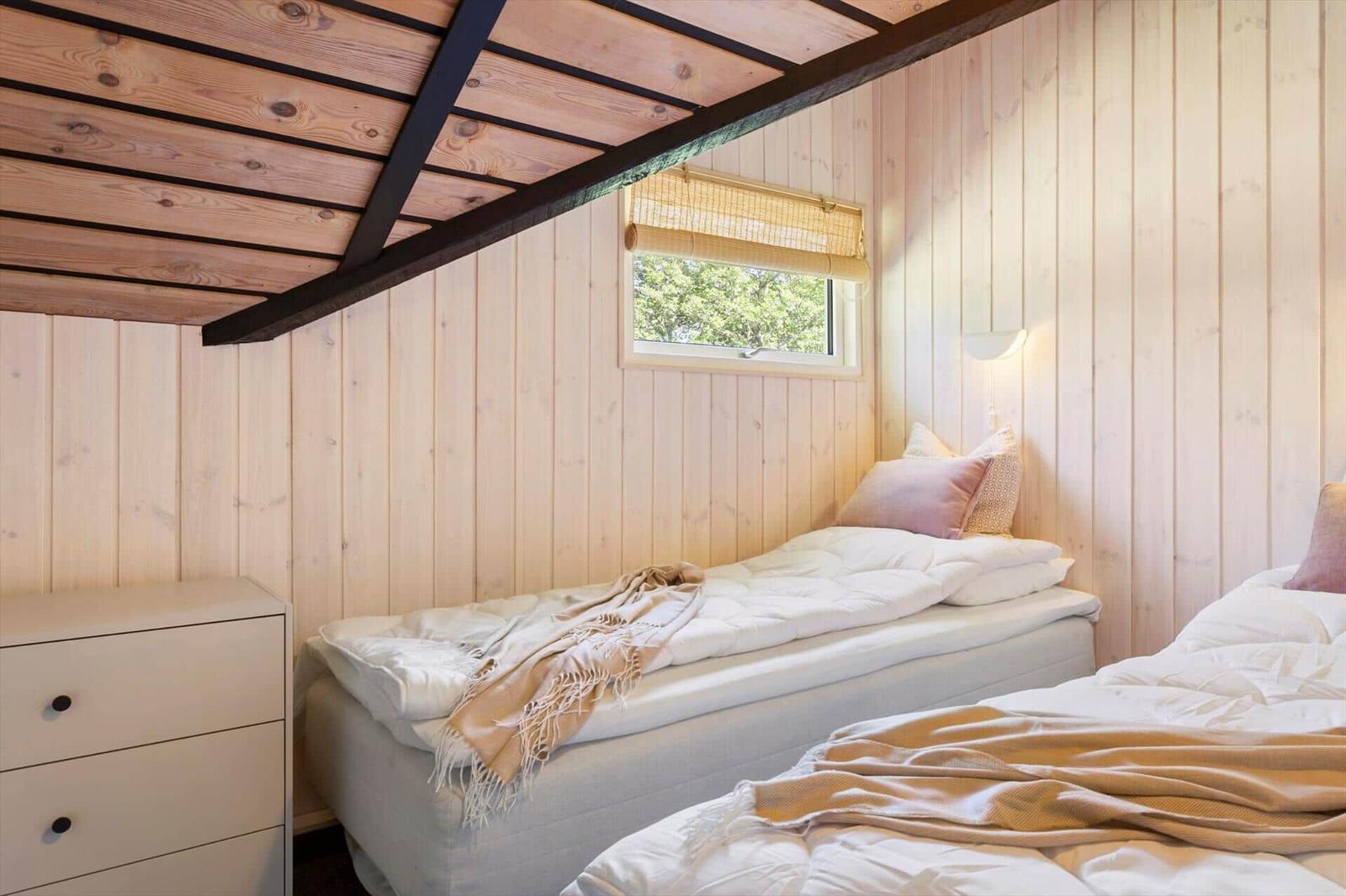 Zwei Betten in einem Holzhauszimmer mit Fenster und Schrank.