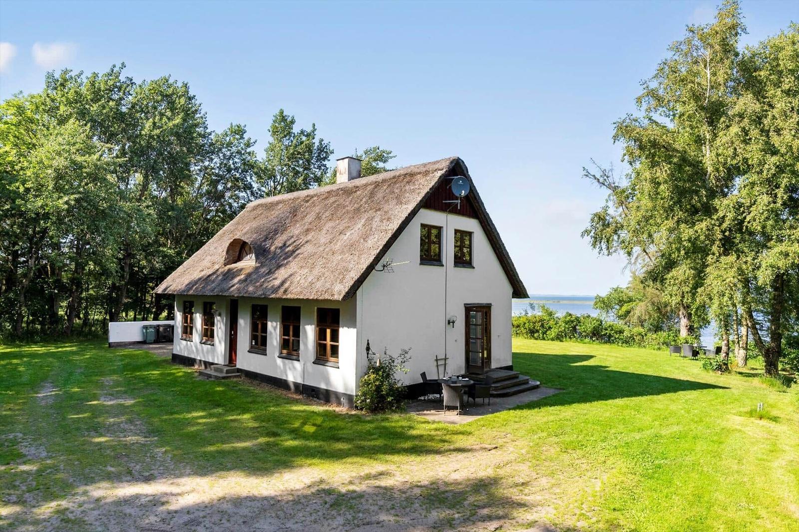 Wohnhaus mit Strohdach, Garten und Blick auf Wasser.