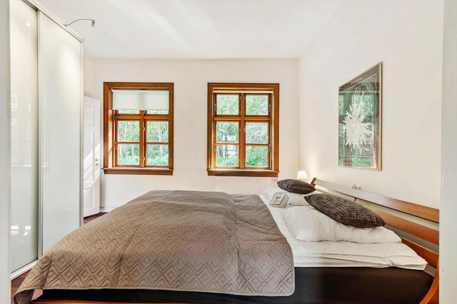 Schlafzimmer mit Bett, zwei Fenstern und Kleiderschrank. Wandbild an der Wand.