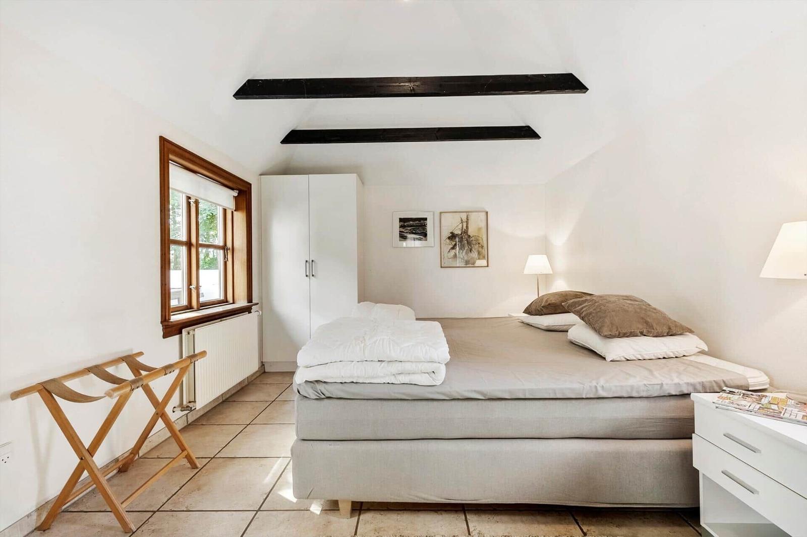 Schlafzimmer mit Bett, Kleiderkabinett und Fenster. Holzgestell und weiße Möbel.