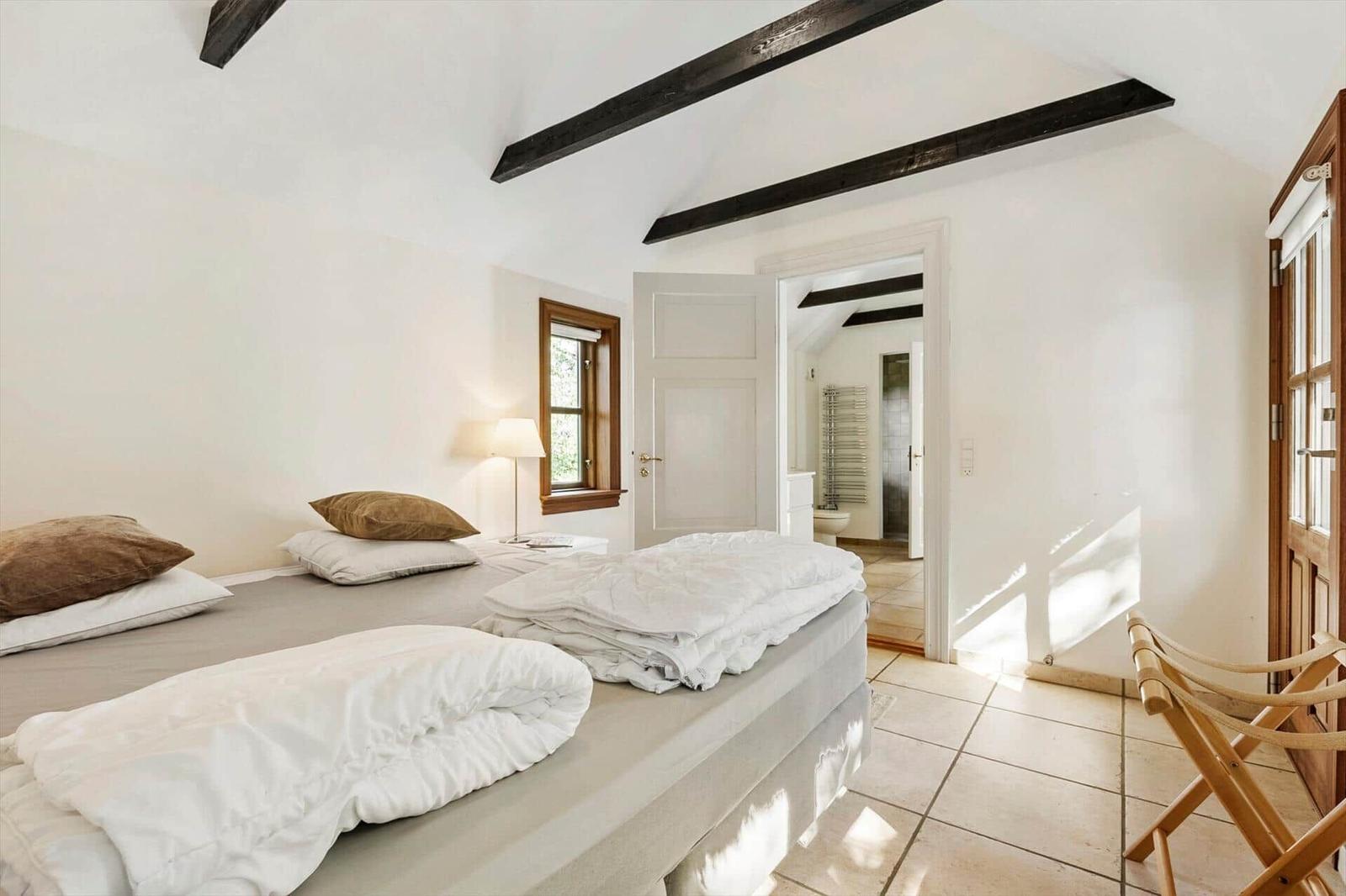Schlafzimmer mit Bett, Fenster und Tür zum Bad.