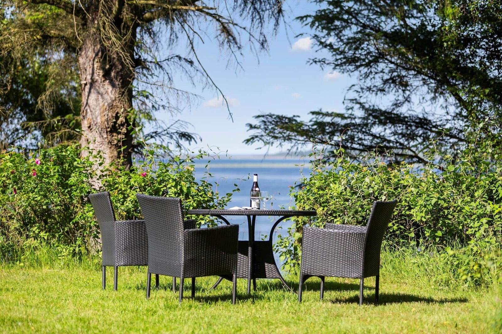 Garten-Tisch mit vier Stühlen vor Wasser und Bäumen