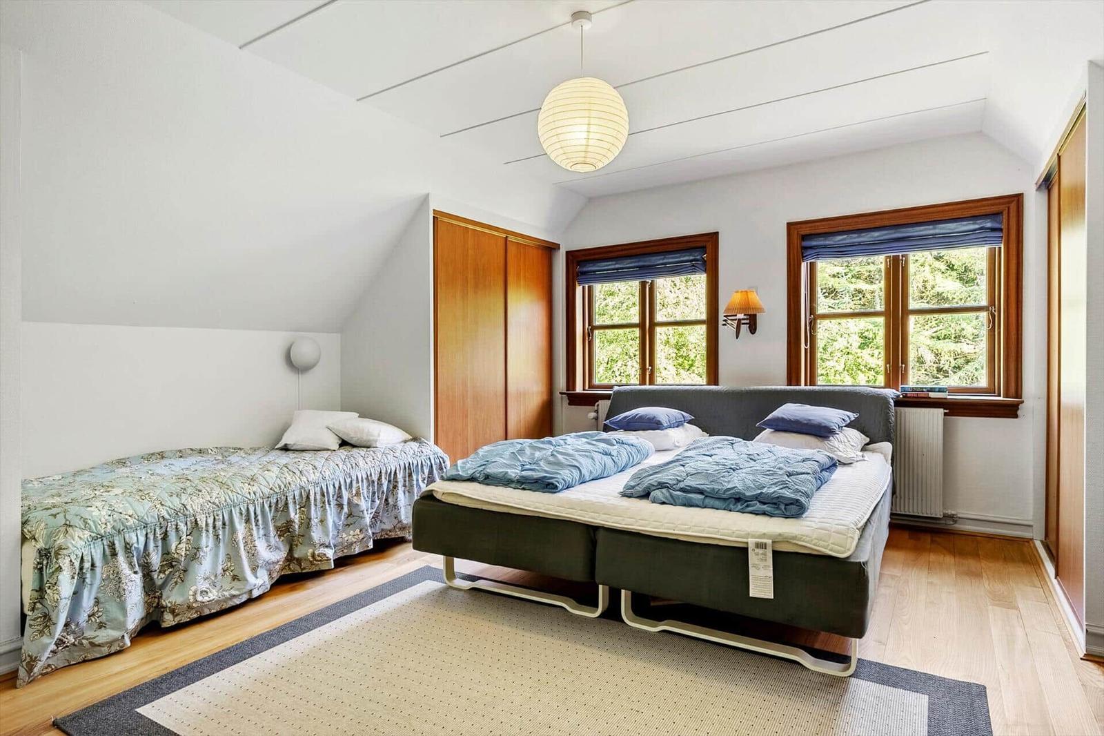 Zimmer mit Doppelbett und Einzelbett, Holzboden und zwei Fenster mit Blick auf Bäume.
