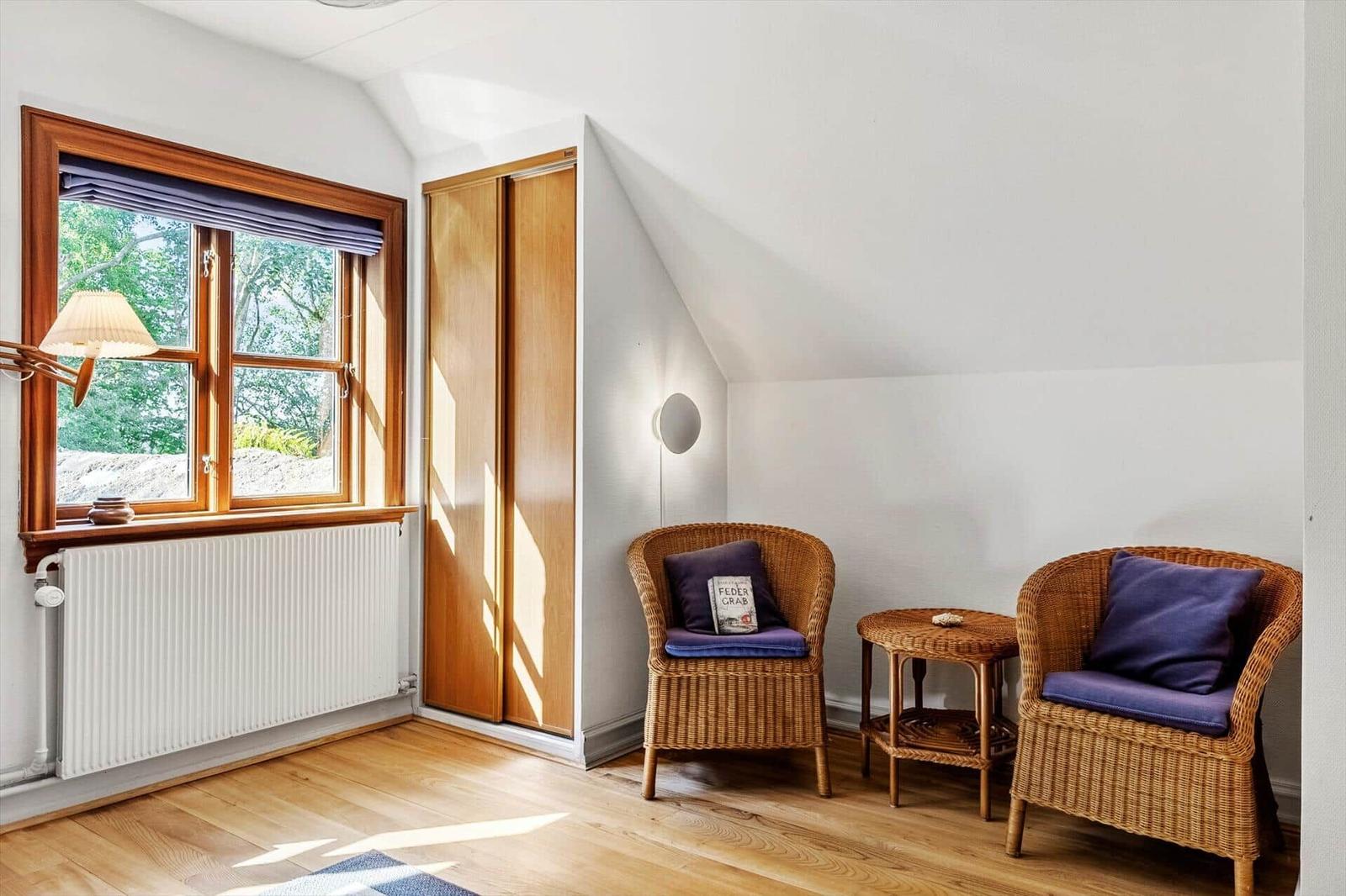 Zimmer mit zwei Rattan-Stühlen, kleinem Tisch und Fenster mit Blick auf Bäume.