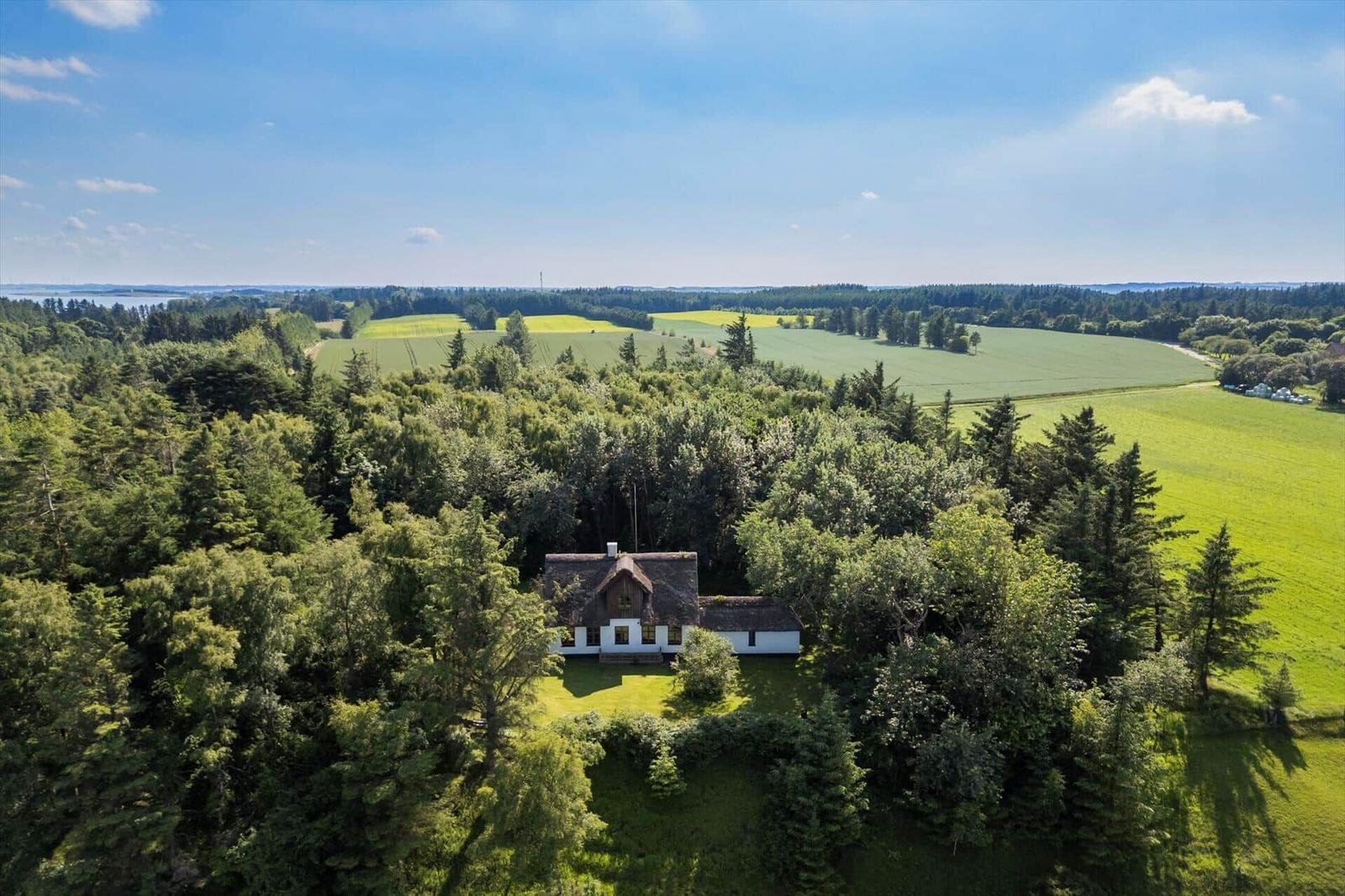 Haus mit Dach und weißen Wänden inmitten von Wald und Feldern.