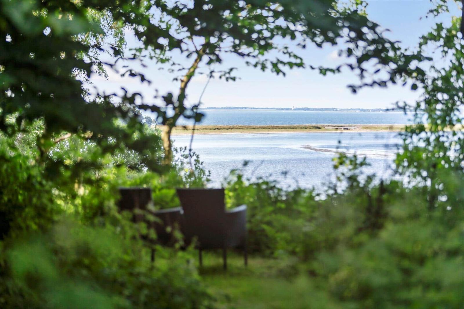 Zwei Stühle im Grünen mit Blick auf Wasser und Strand.