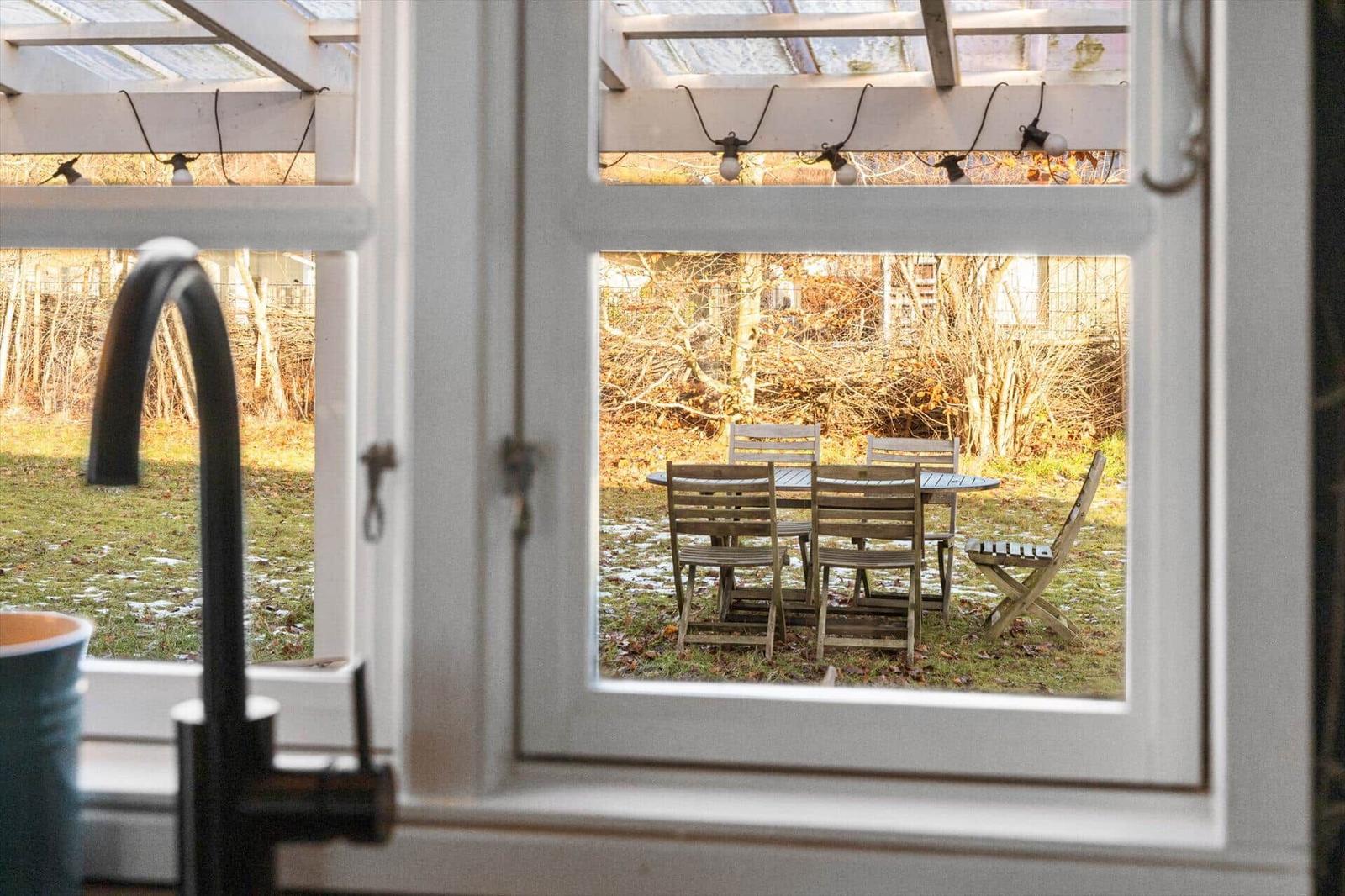 Durch das Fenster ist ein Garten mit Tisch und Stühlen zu sehen.