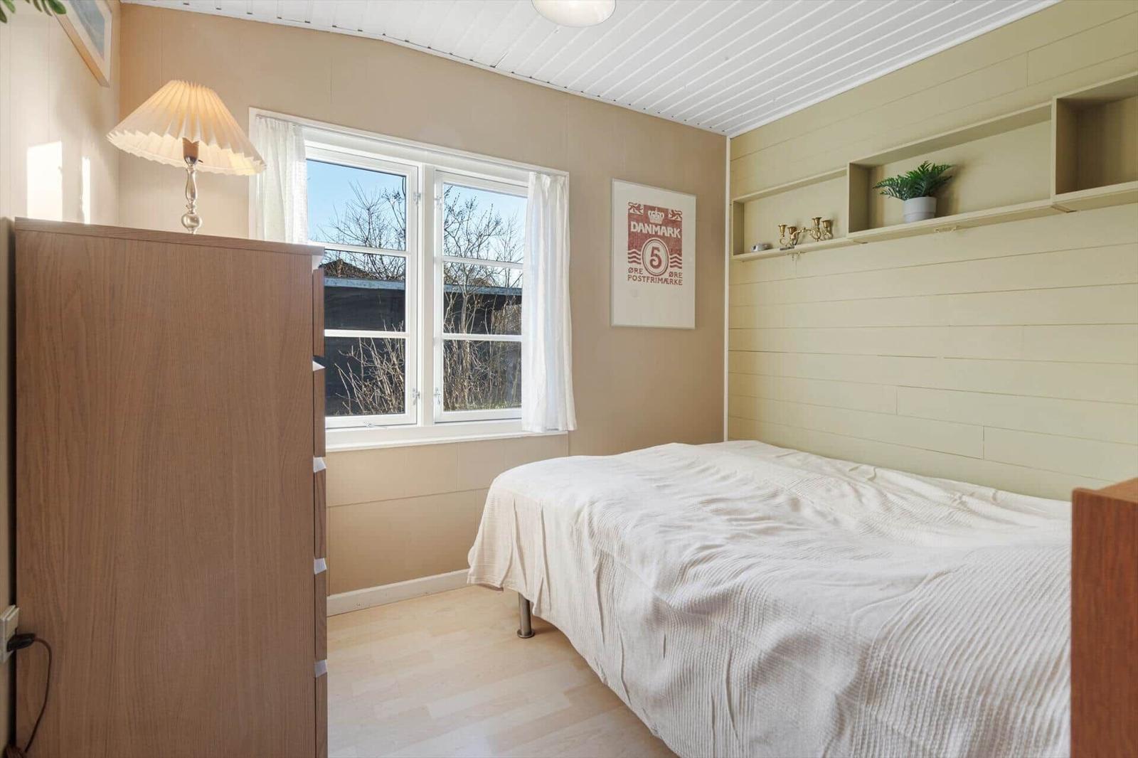 Schlafzimmer mit Bett, Fenster, Schrank und Wandregal.