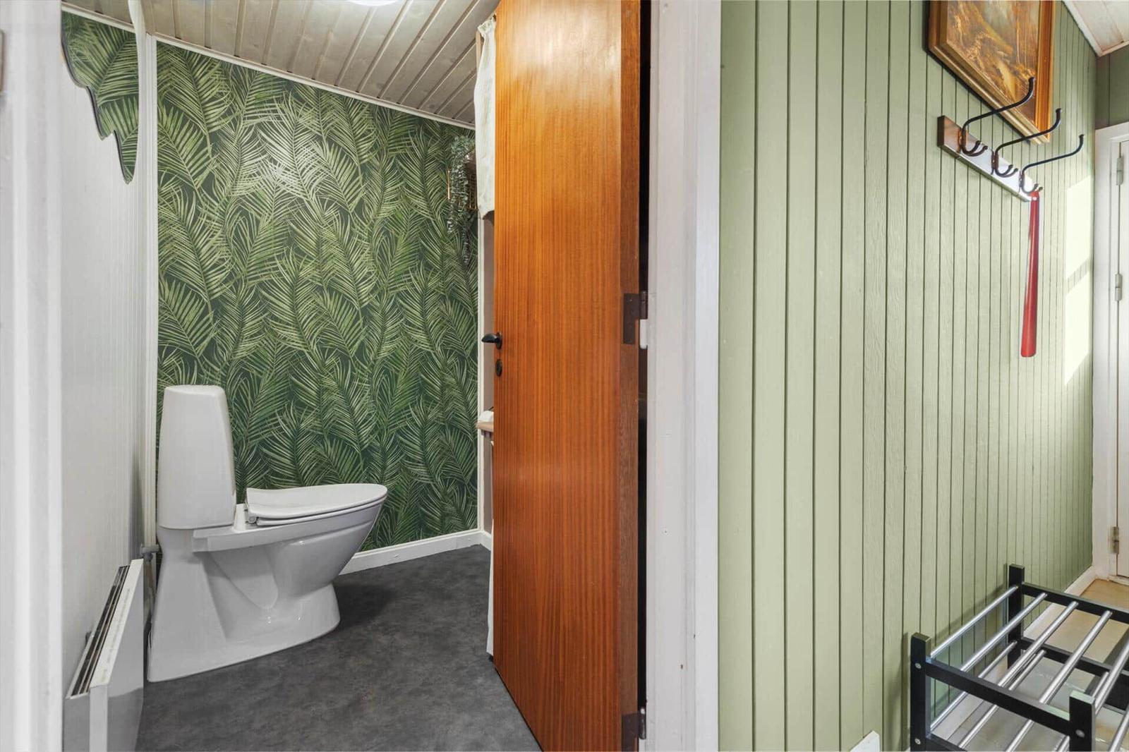 Toilettenbereich mit Palmen壁纸 und Holztür. Grüne vertikale Wandverkleidung und Kleiderhaken.