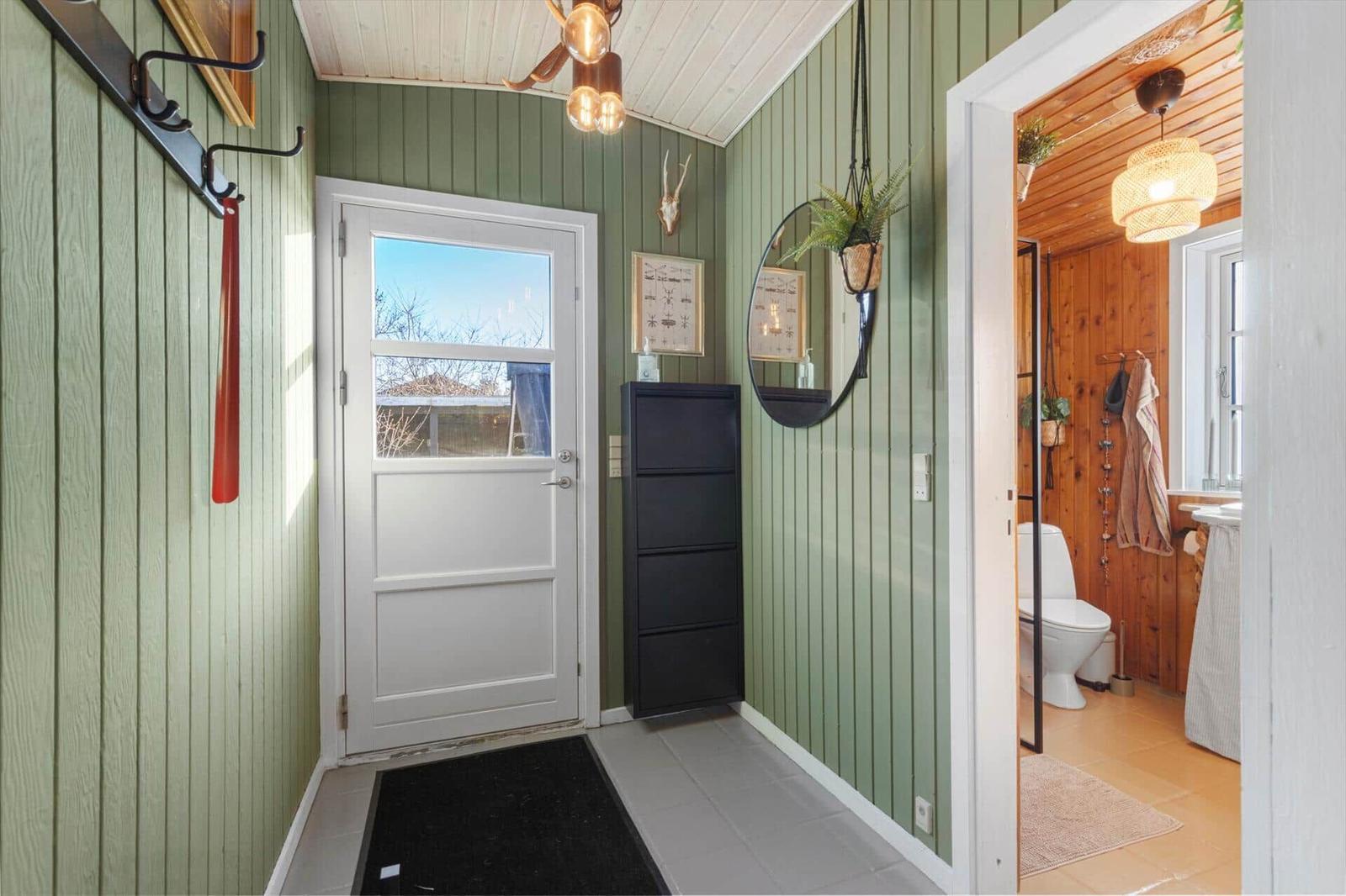 Eingangsbereich mit grünen Wänden, weiße Tür und Blick in die Toilette.