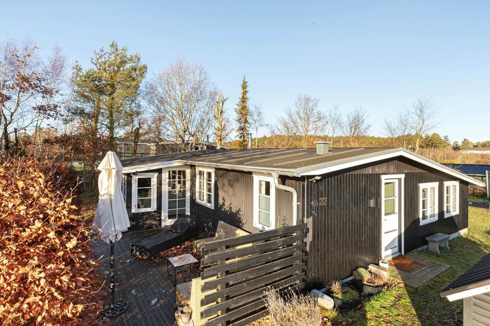 Ein dunkel lackiertes Holzhaus mit weiß gerahmten Fenstern und einer Terrasse mit Sonnenschutz.