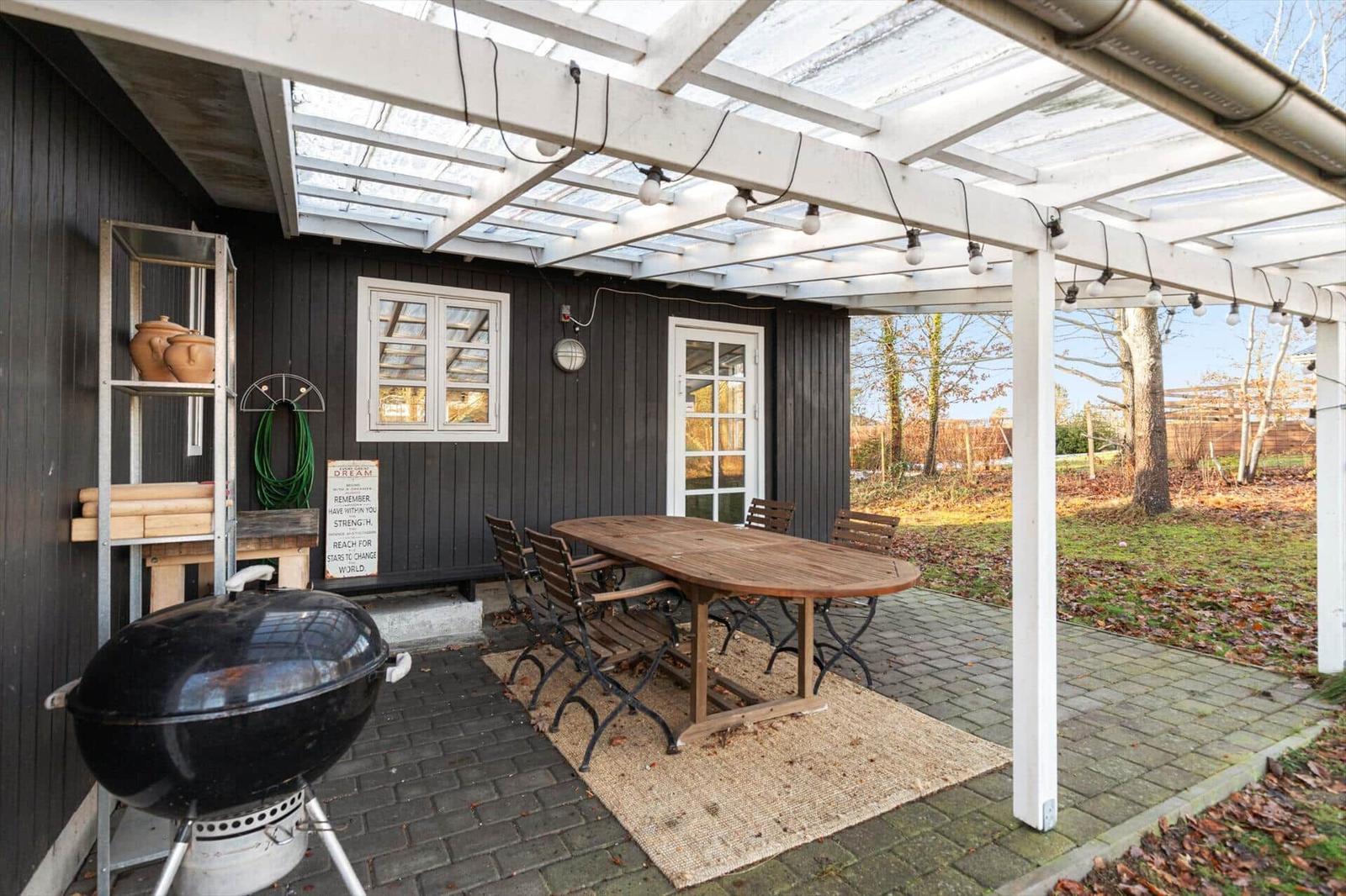 Terrasse mit Tisch, Stühlen und Grill unter einem weißen Dach.