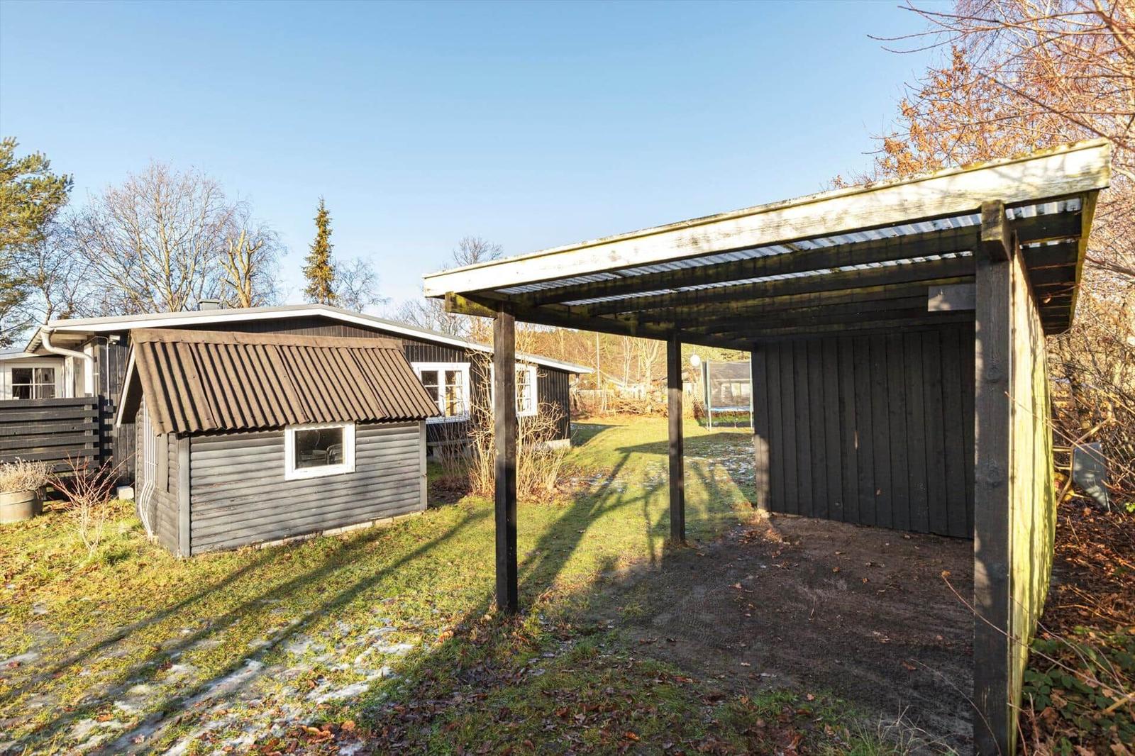 Hinterhof mit Holzüberdachung und kleinem Schuppen. Grasfläche und Bäume im Hintergrund.