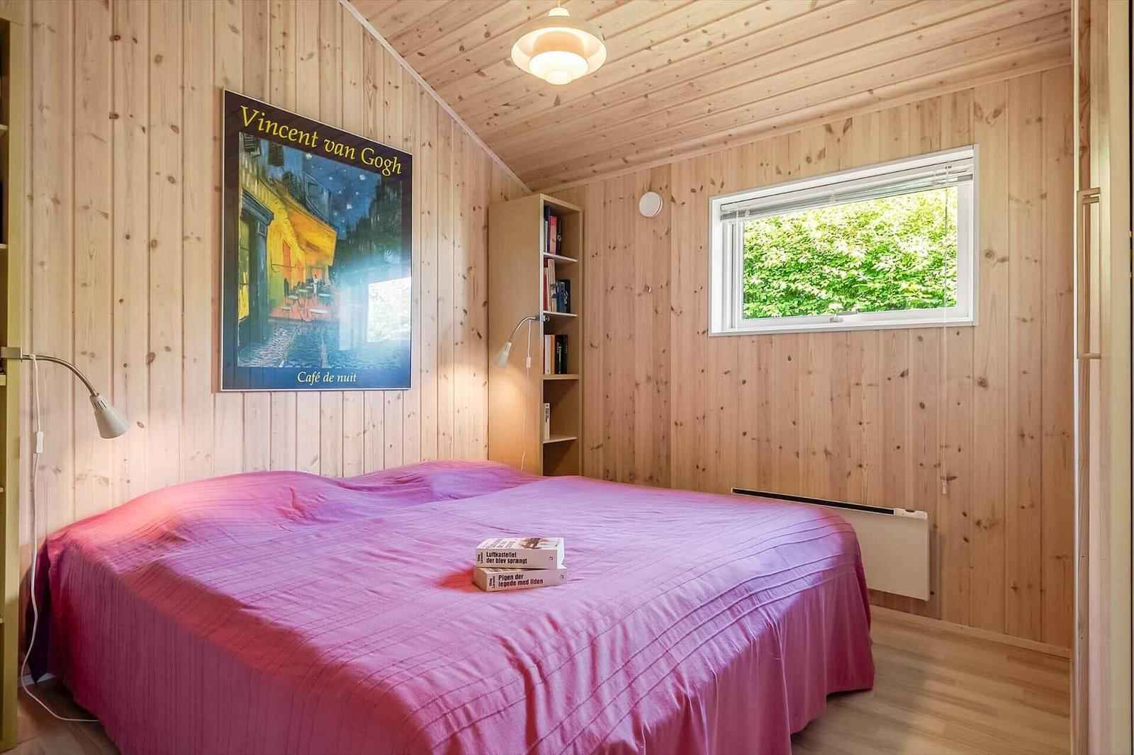 Schlafzimmer mit Holzwänden, Bett mit rosa Bettwäsche und Wandbild von Vincent van Gogh.