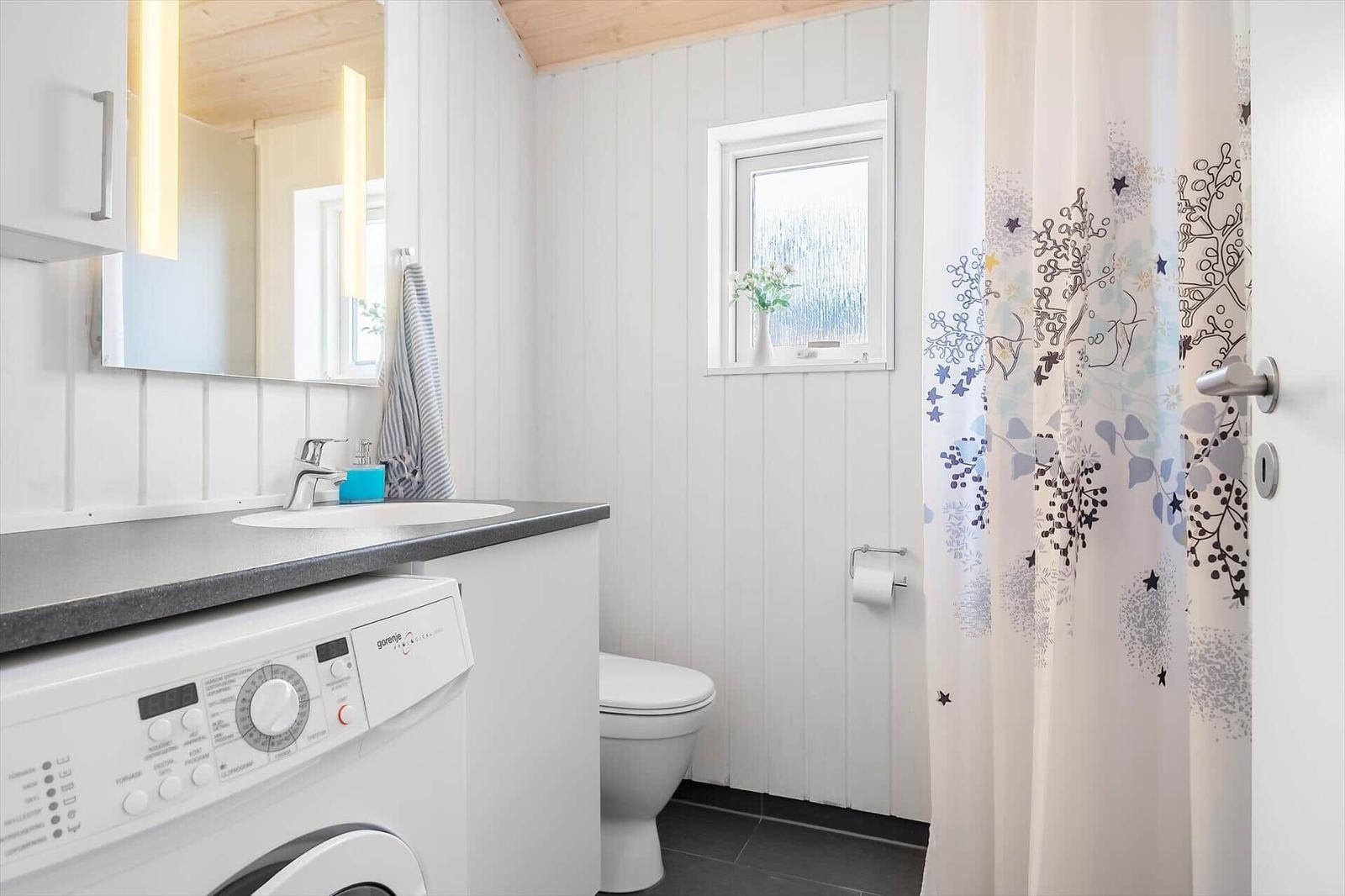 Badezimmer mit Waschmaschine, Toilette und Duschvorhang mit Muster.