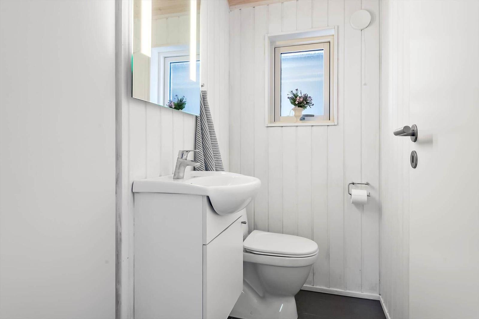 Badezimmer mit Waschbecken, Toilette und kleinem Fenster mit Blumen.