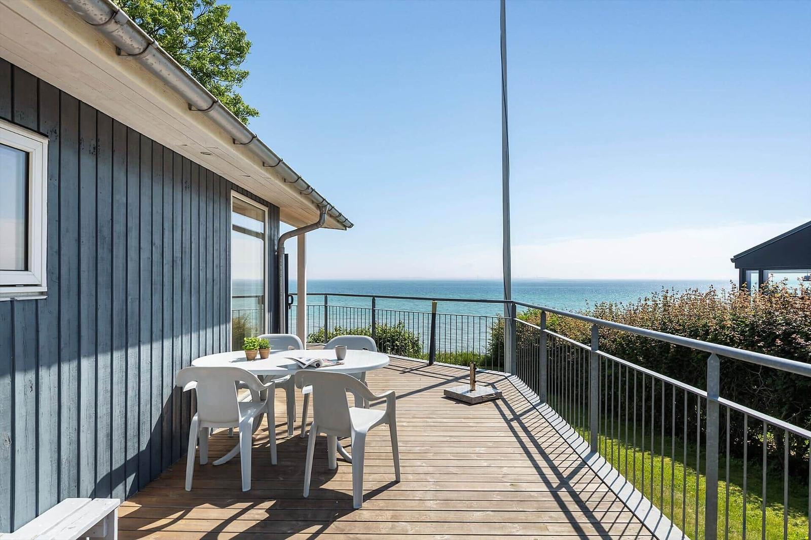 Terrasse mit Tisch und Stühlen bietet Meerblick. Holzdeck und Metallgeländer.
