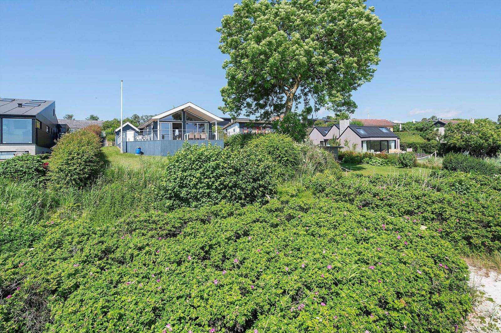 Haus mit Balkon und Garten, umgeben von Grün und Bäumen unter blauem Himmel.