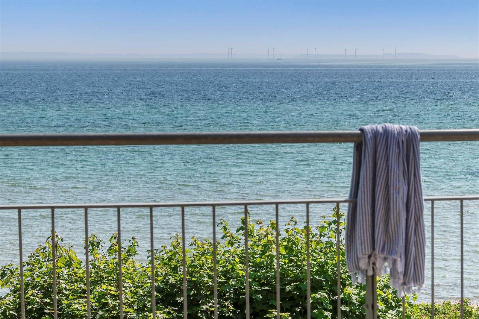 Balkon mit Blick auf das Meer und Windkraftanlagen im Hintergrund. Ein Handtuch hängt am Geländer.