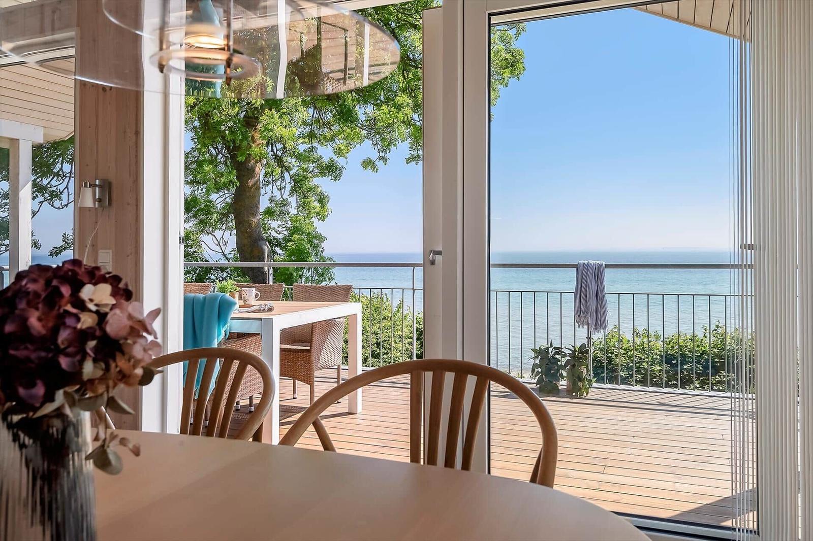 Terrasse mit Meerblick, Tisch und Stühle, Blick durch Glastüren ins Innere.