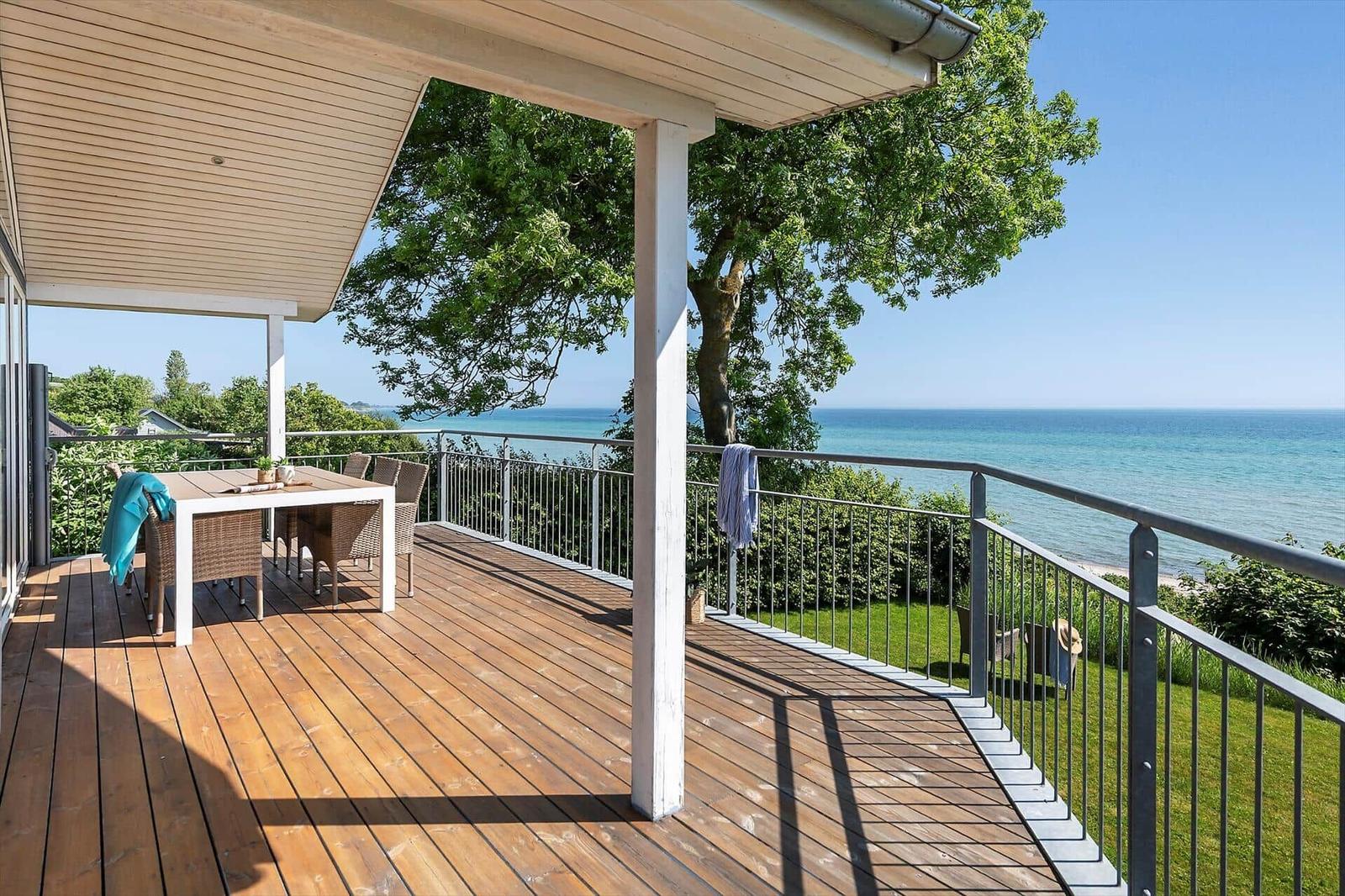 Terrasse mit Tisch und Stühlen, Blick auf das Meer und grüne Bäume.