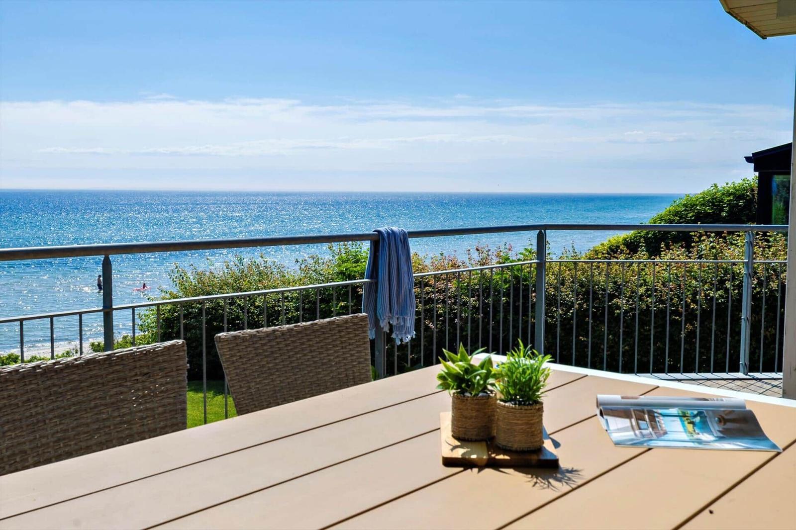 Terrasse mit Tisch, Stühlen und Meerblick. Blau gestreiftes Handtuch hängt am Geländer.