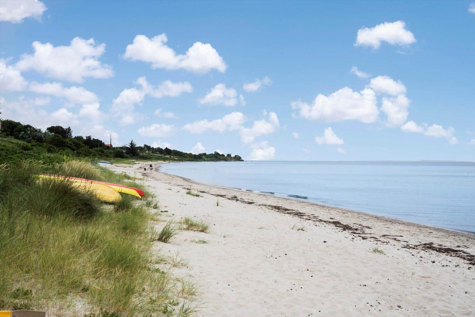 Strand mit Sand, Gras und einem roten Kanu unter blauem Himmel mit weißen Wolken.