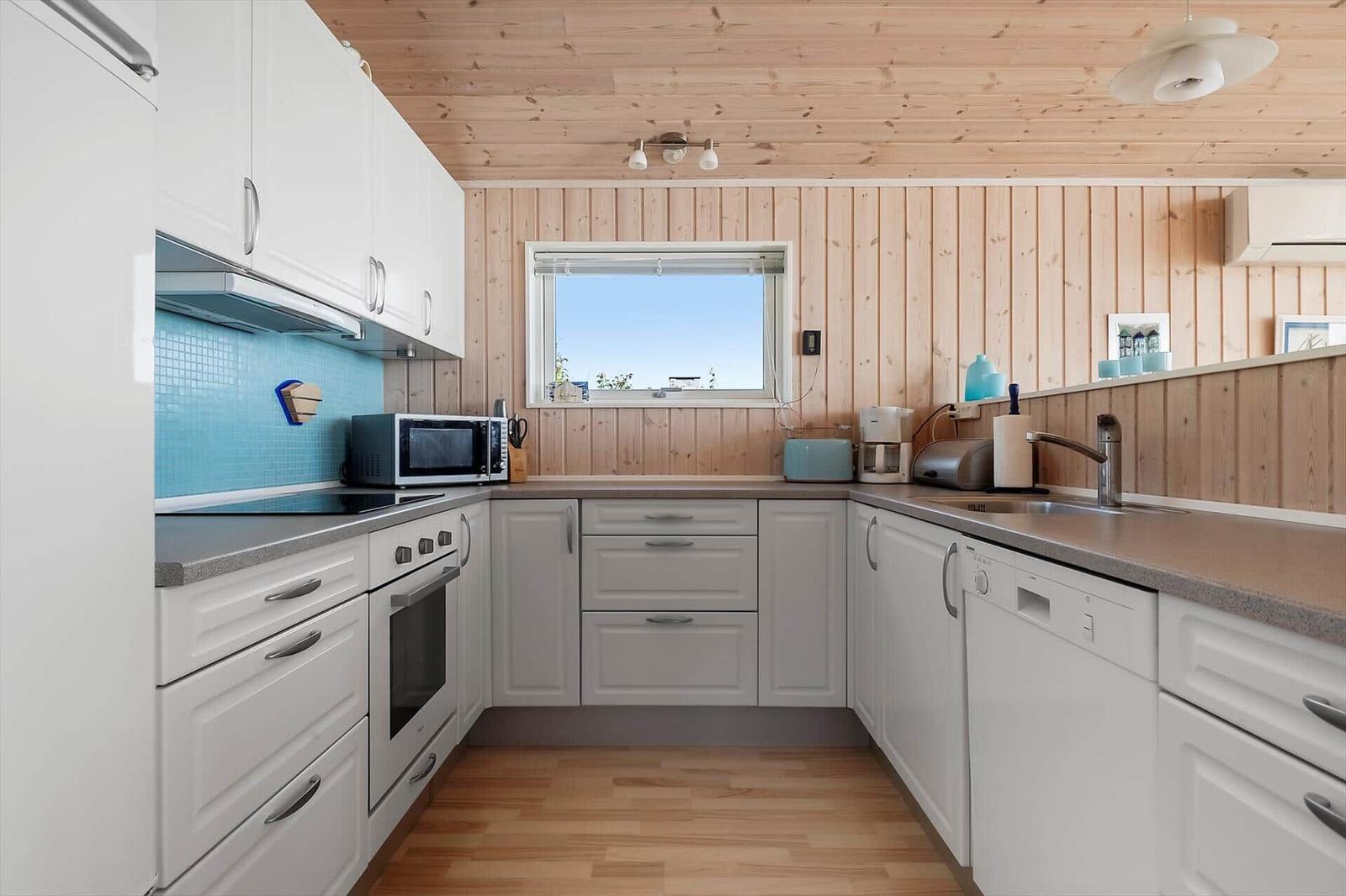 Küche mit weißen Schränken, Holzdecke und Fenster mit Blick nach draußen.
