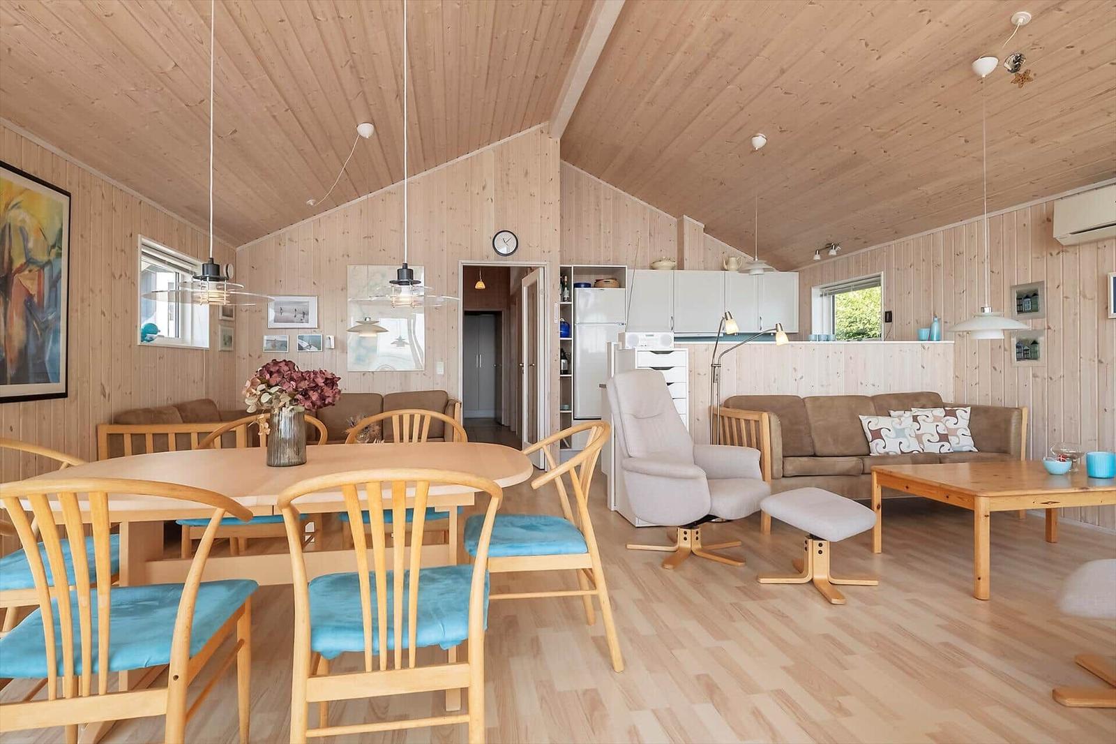 Ein Raum mit Essbereich und Wohnbereich, Holzwand und -decke, Holzfußboden, Esstisch mit Stühlen und Sofa.
