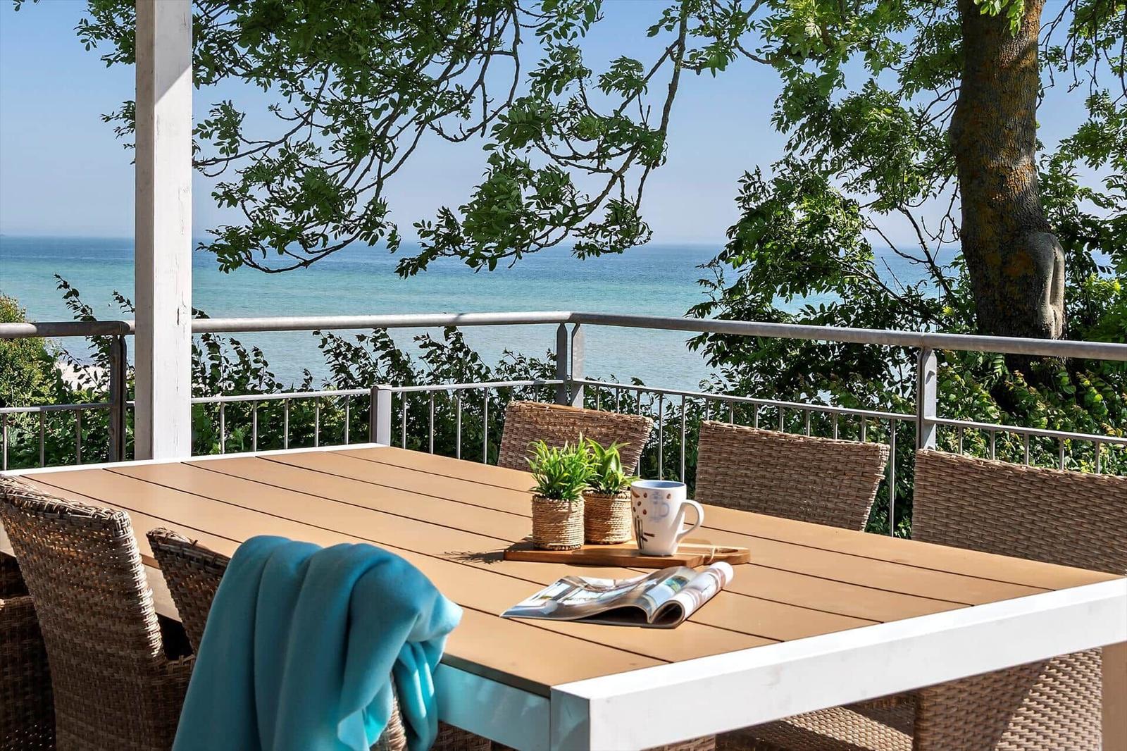 Terrasse mit Tisch und Stühlen, Blick auf das Meer und Bäume.
