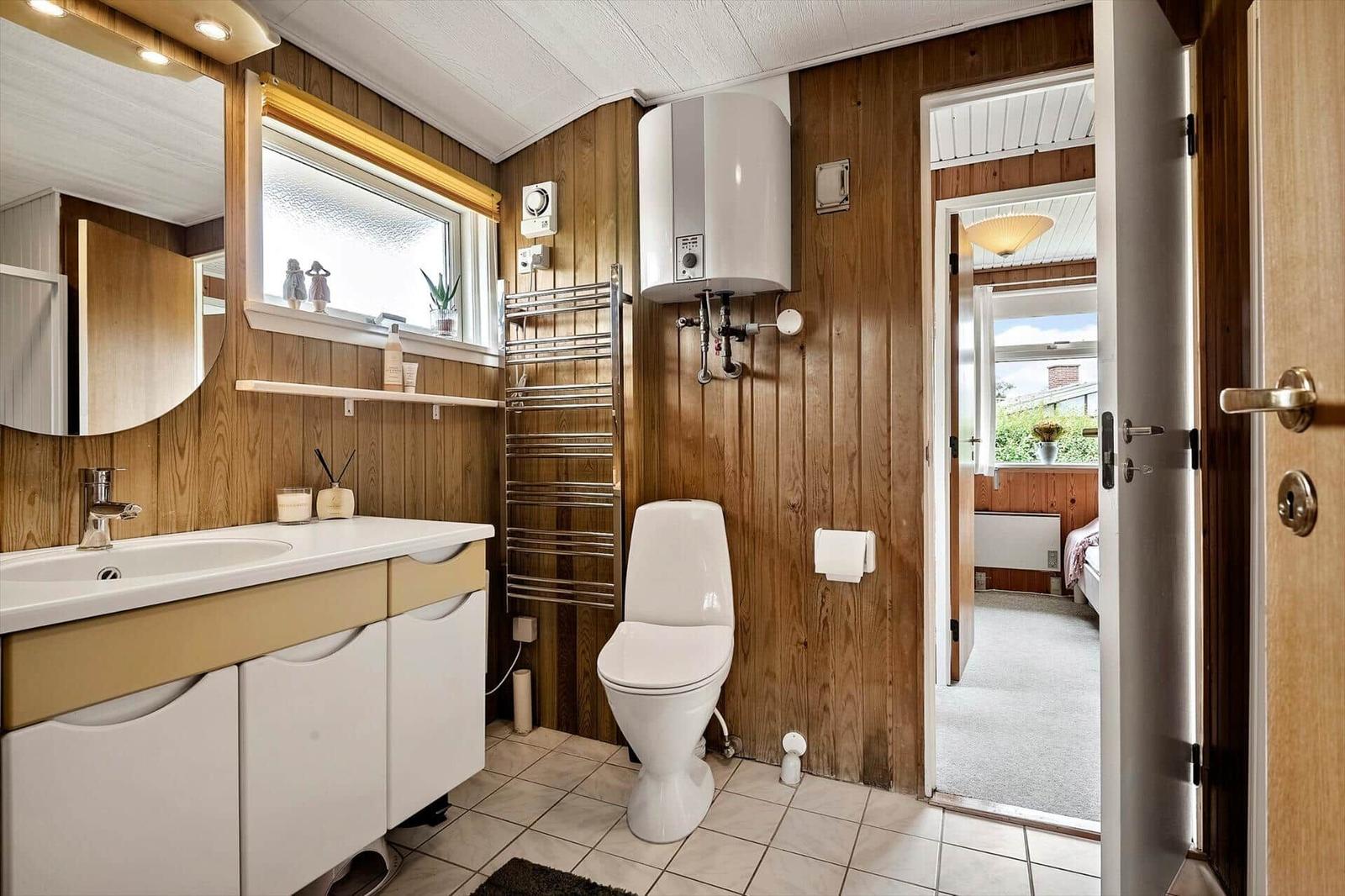 Badezimmer mit Waschbecken, Toilette und Badewannenheizung. Holzwandverkleidung und Fenster mit Blick.