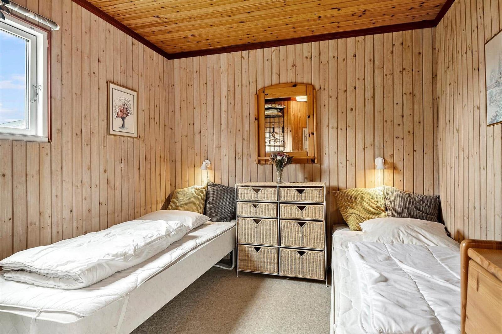 Zwei Einzelbetten mit weißen Bettwäschen, Holzwände und ein Schrank mit Körben.