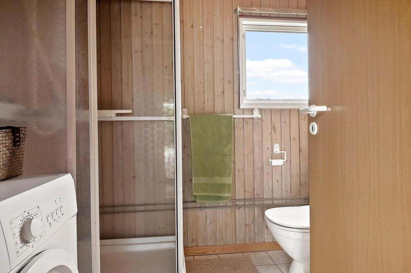 Badezimmer mit Dusche, Toilette und Waschmaschine. Holzwände und kleines Fenster.