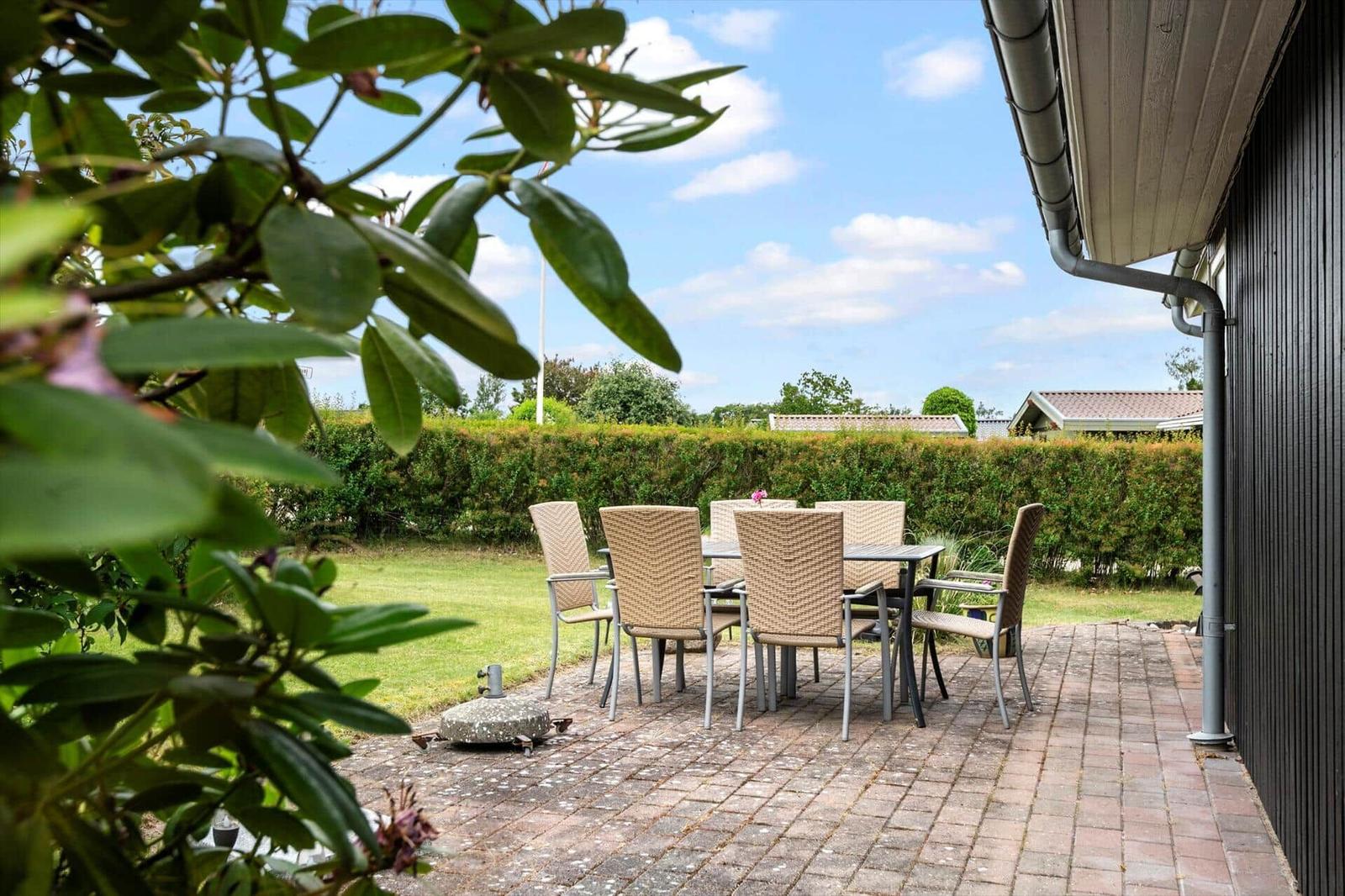 Terrasse mit Sitzgruppe, Grill und Grünfläche. Blick auf Hecke und Himmel.