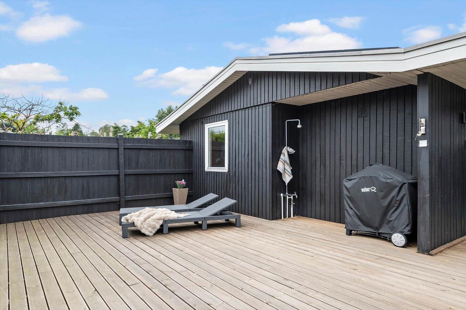 Terrasse mit Liegestühlen, Dusche und Grill, umgeben von Holzgeländern.