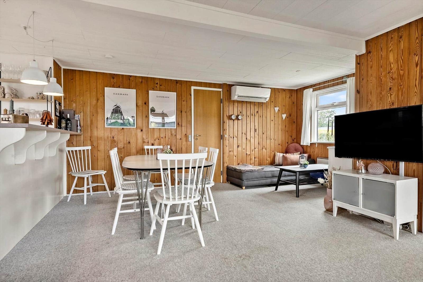 Wohn- und Essbereich mit Holzwänden, Esstisch, Sofa und Fernseher.