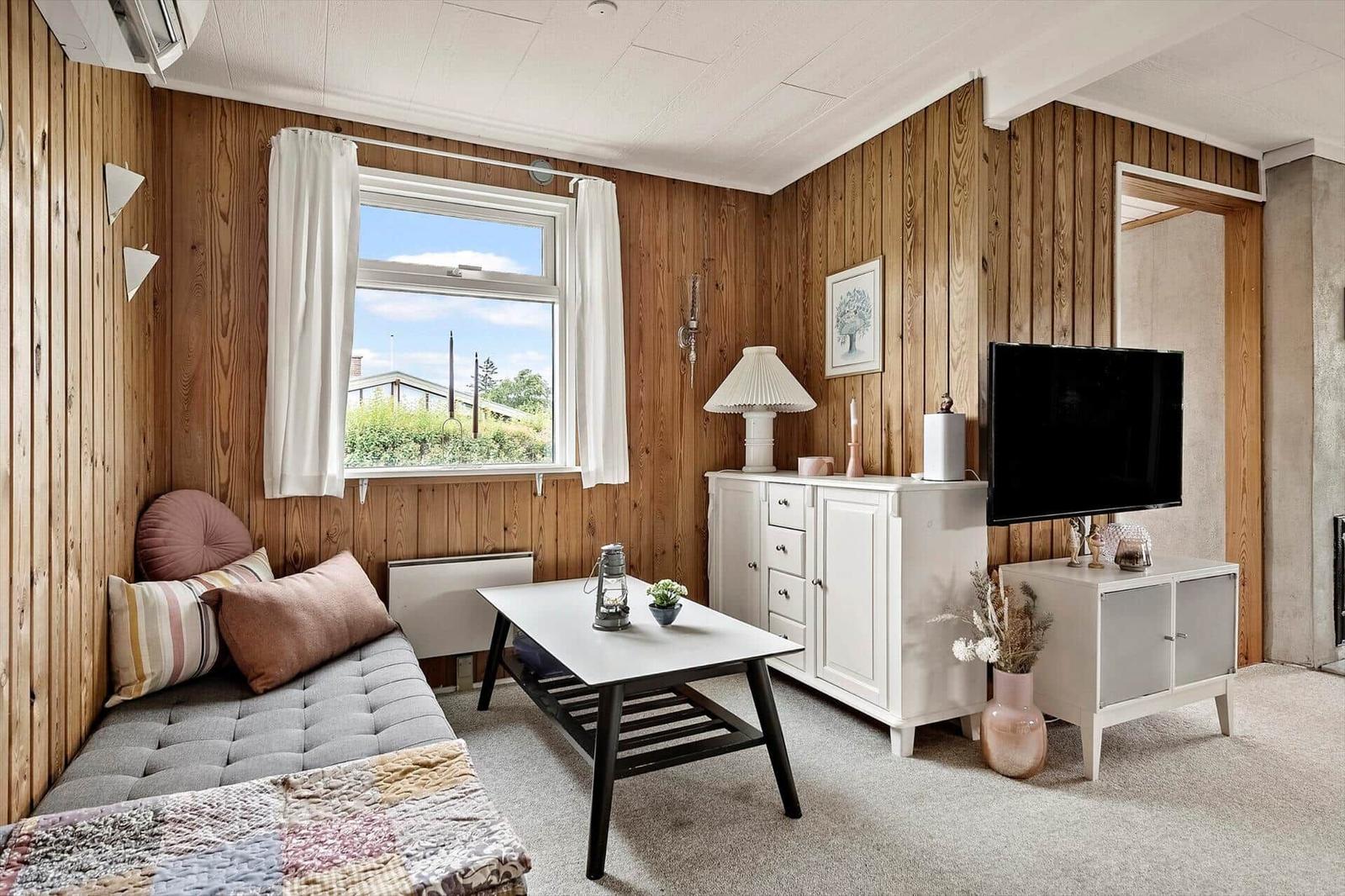 Ein Raum mit Holzwänden, Fenster, Sofa, Couchtisch und Fernseher.