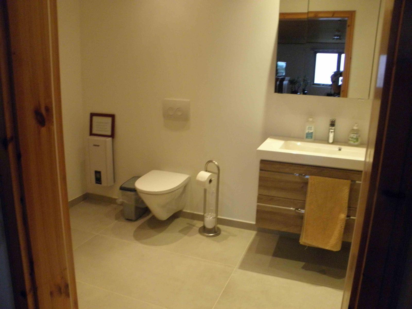 Badezimmer mit Toilette, bodentiefer Dusche, Wandwaschbecken und 2 Schubladen, in denen sich Handtücher und diverse andere Dinge befinden