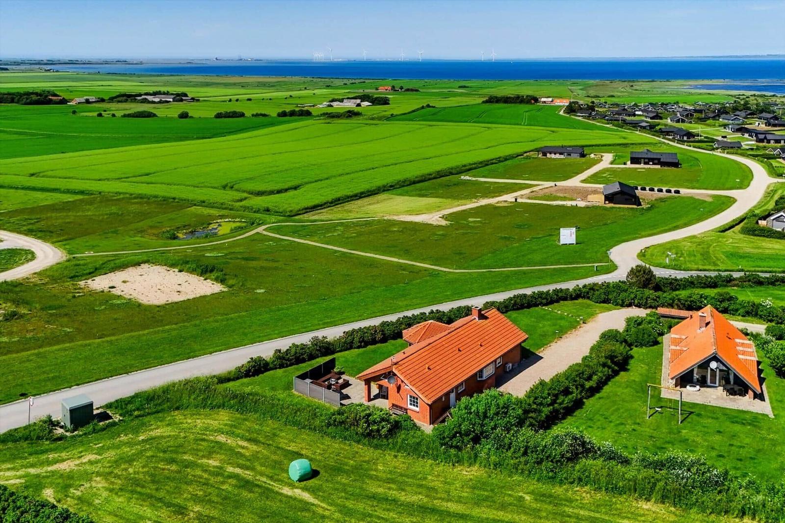 Haus mit rotem Dach, umgeben von grünen Feldern und blauem Meer.