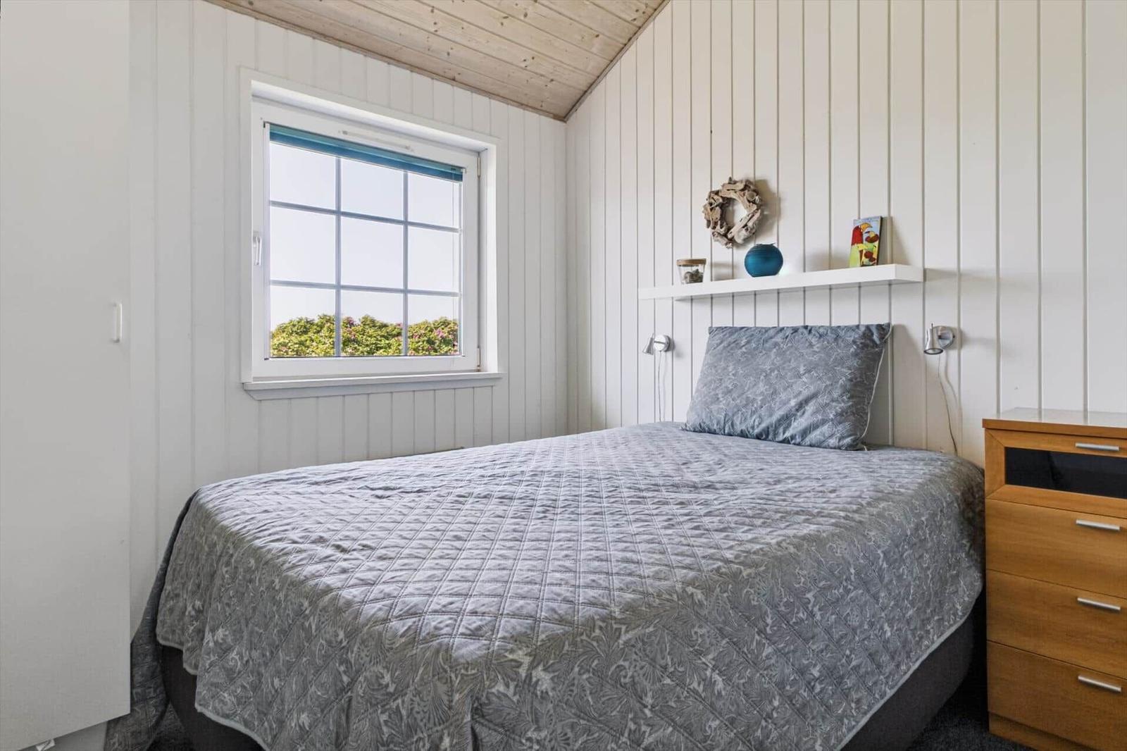 Schlafzimmer mit Bett, Fenster und Nachttisch. Wandverkleidung und Holzdecke.